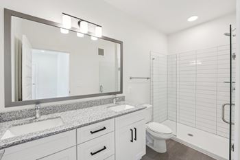 A bathroom with a sink, mirror, toilet and stand up frameless glass shower.